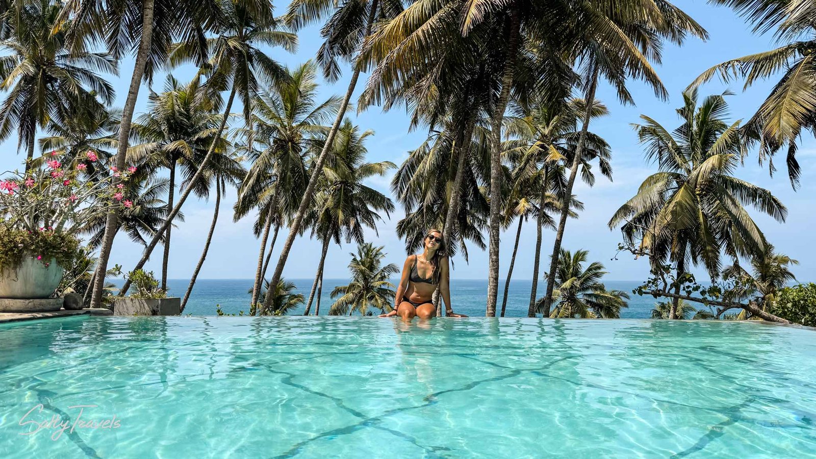 A digital nomad in Sri Lanka relaxing by an infinity pool surrounded by lush palm trees with a stunning ocean view in the background, showcasing the island's serene and tropical work-life balance.